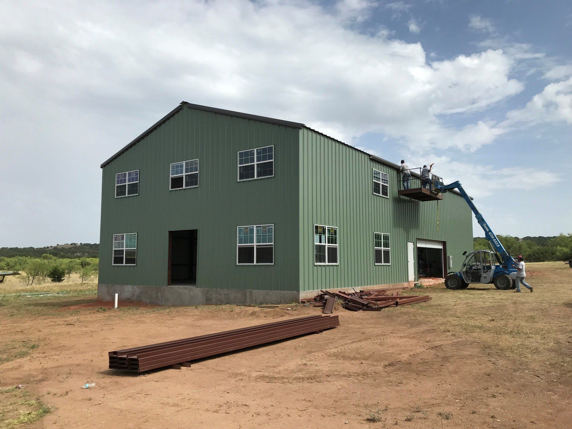 A large green building is being built in a dirt field.