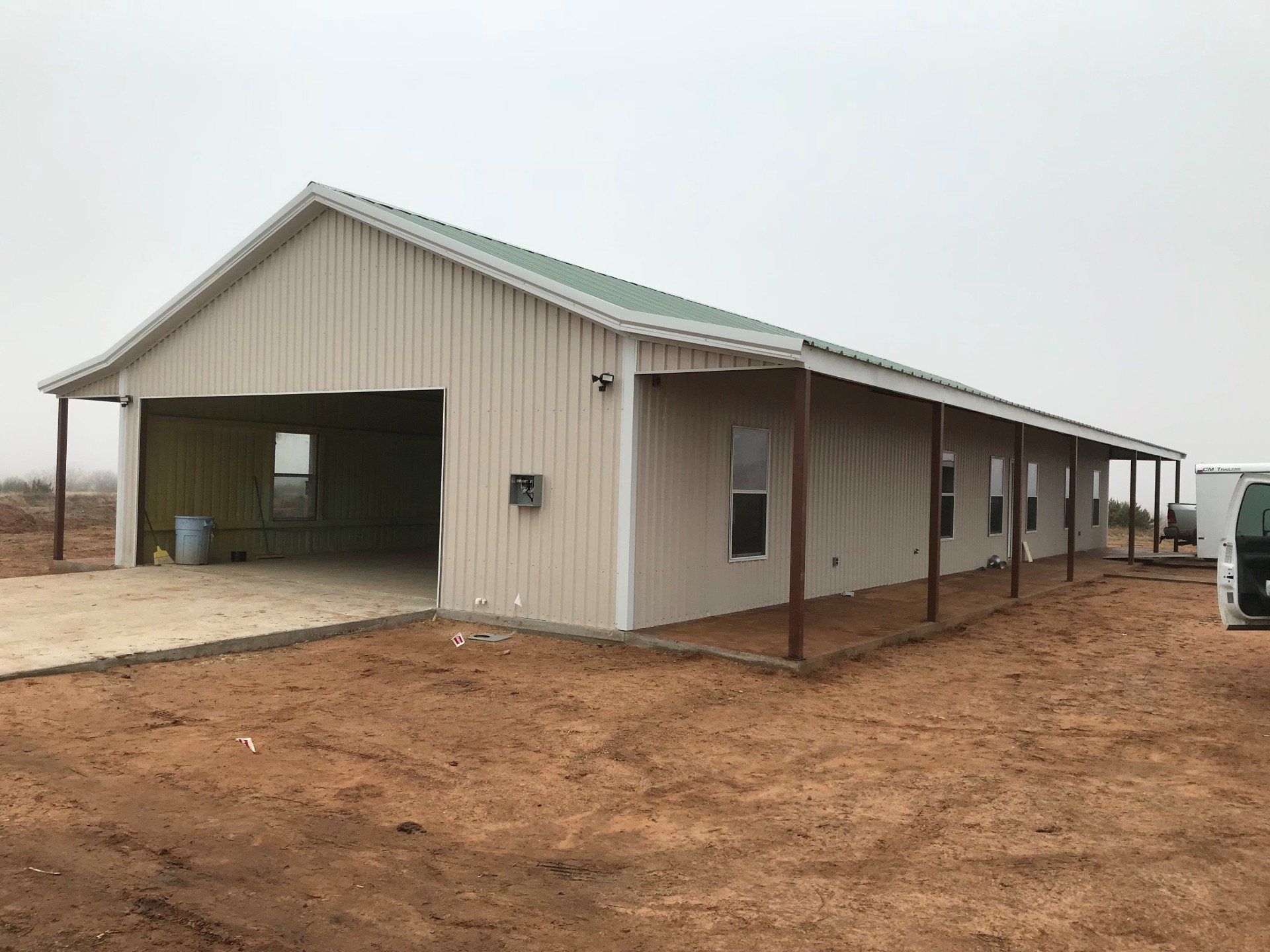 A large building with a green roof is sitting in the middle of a dirt field.