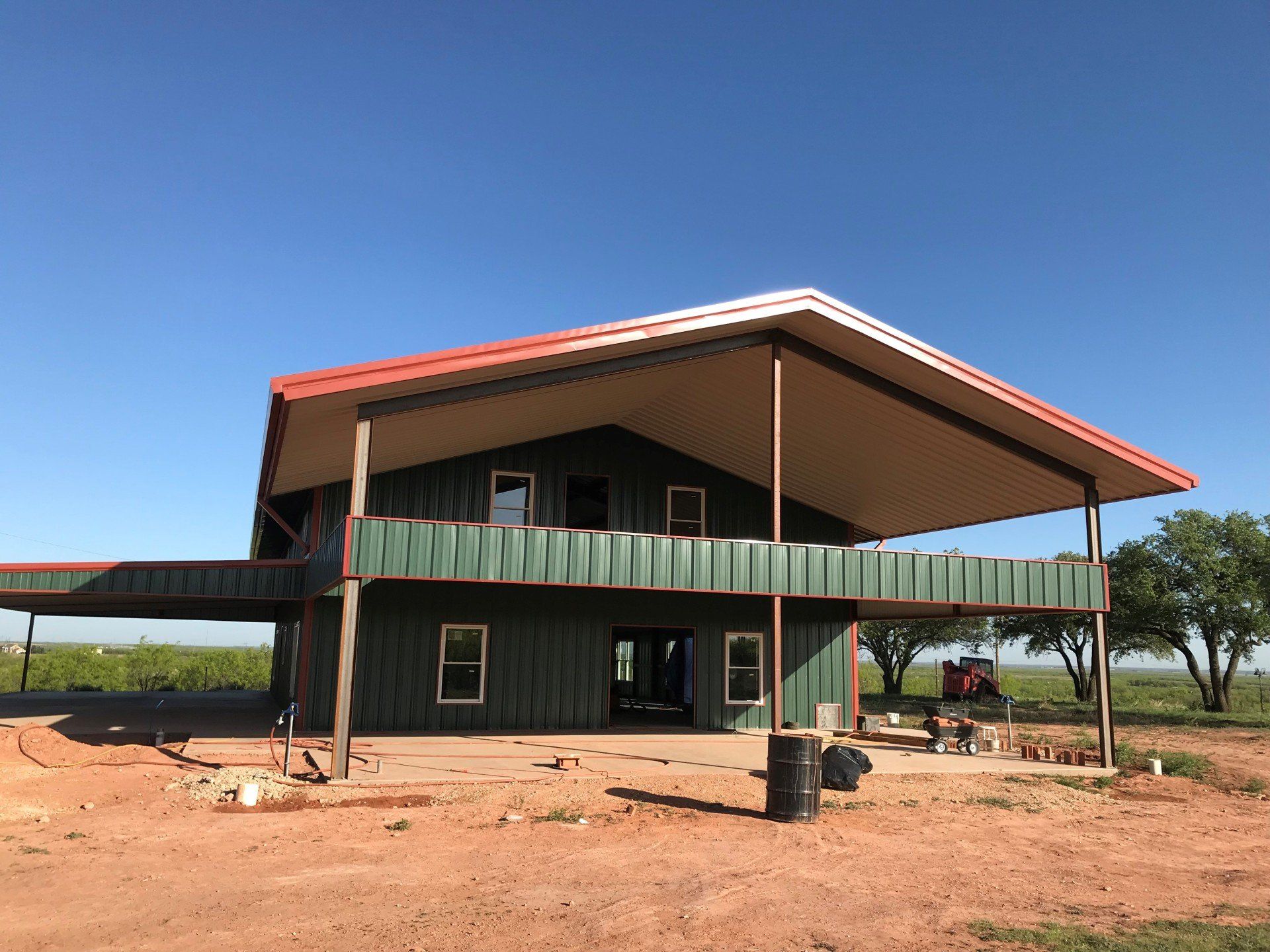 A green house with a red roof is being built in a dirt field.
