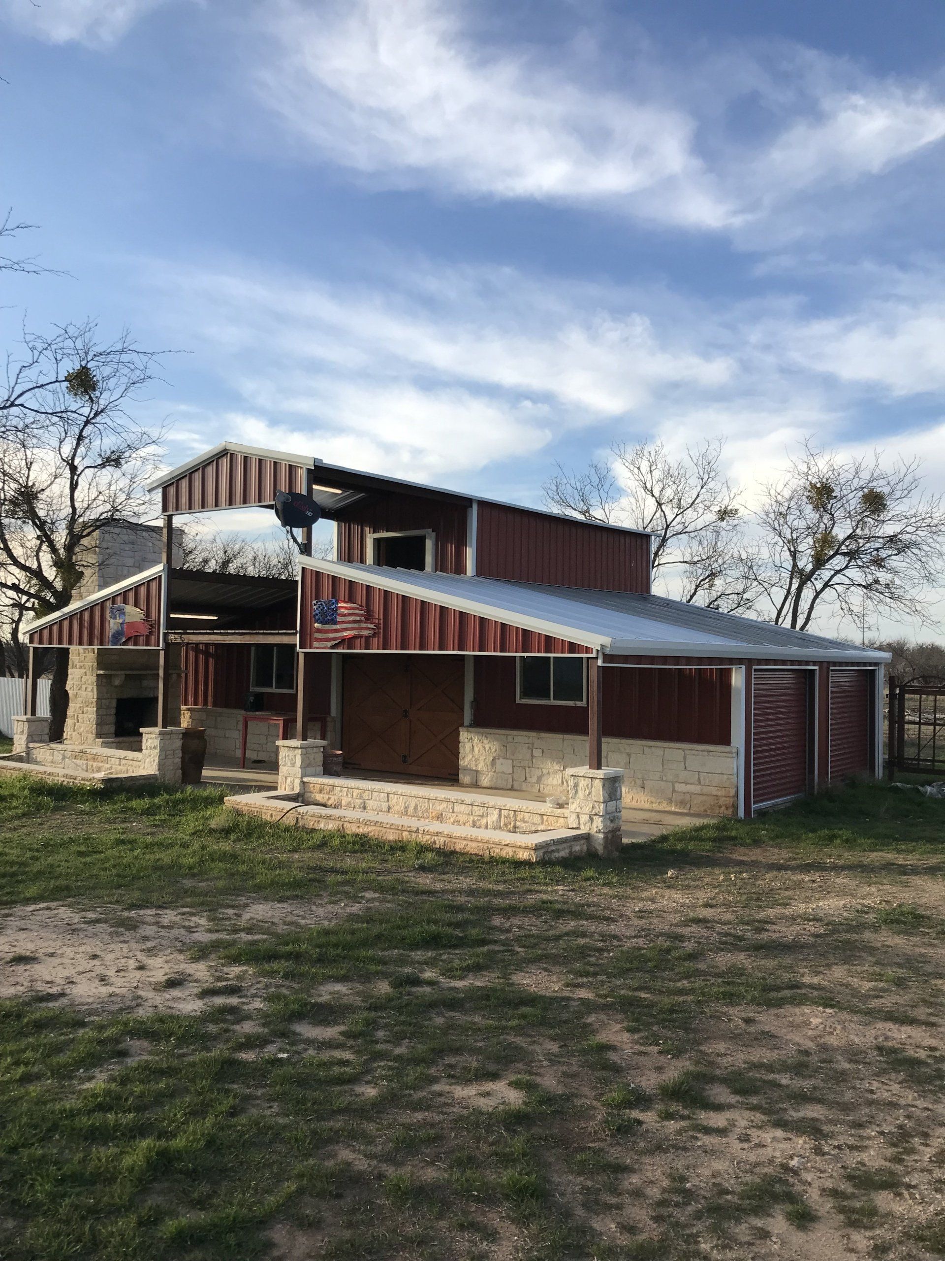 A red barn with a metal roof is sitting in the middle of a grassy field.