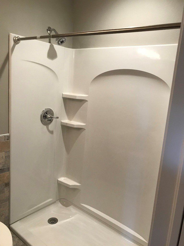 A white shower stall with shelves and a shower head in a bathroom.