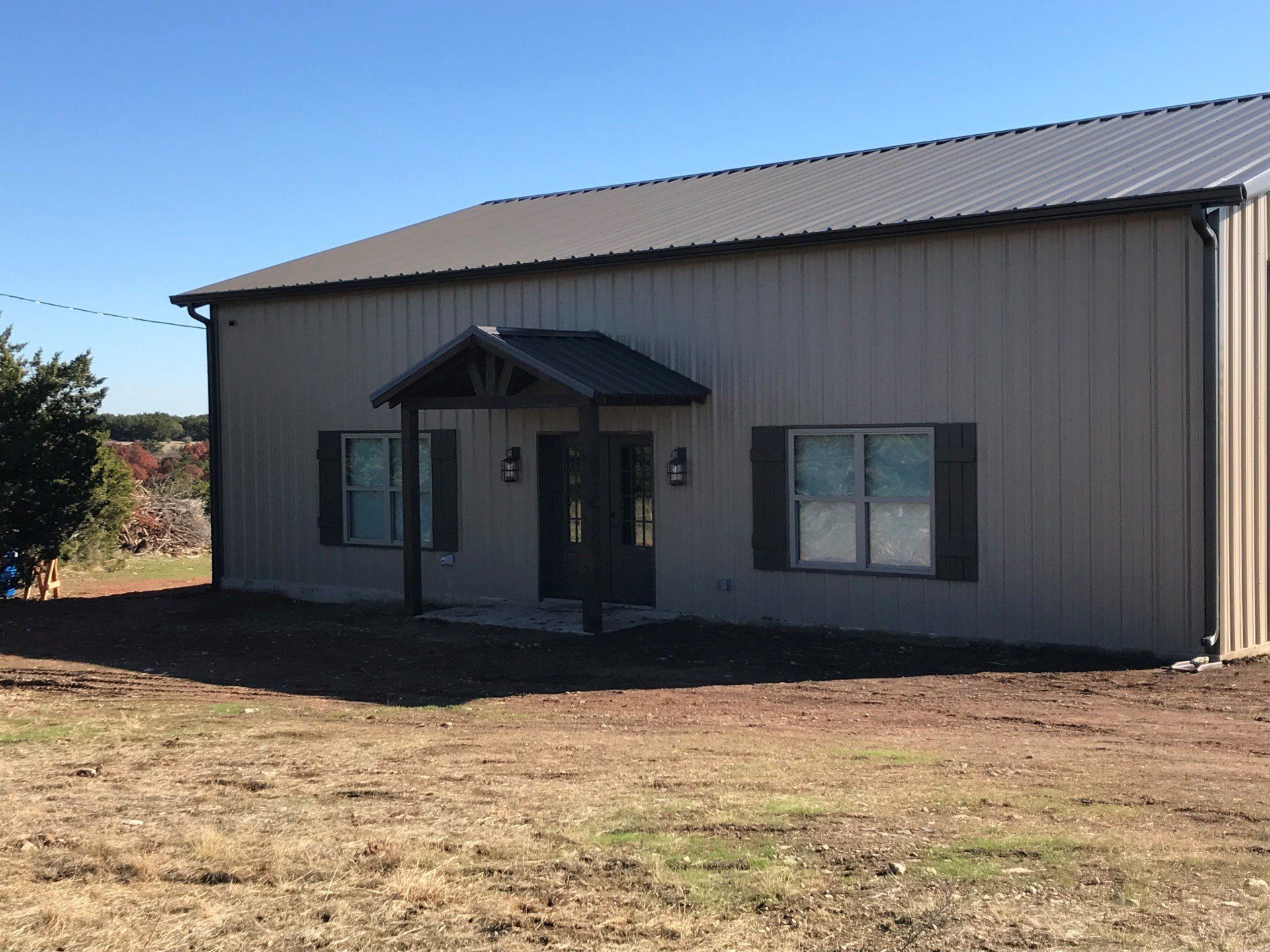 A large metal building with a porch and shutters is sitting in the middle of a field.