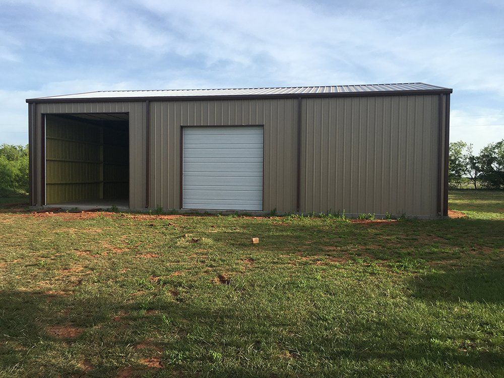 A metal building with a garage door is sitting in the middle of a grassy field.