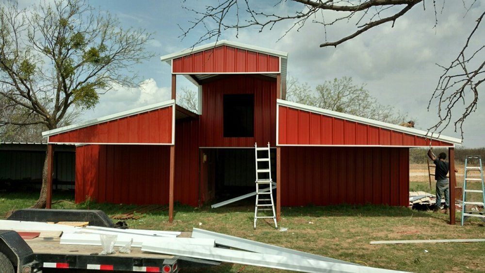 A man is standing in front of a red barn.