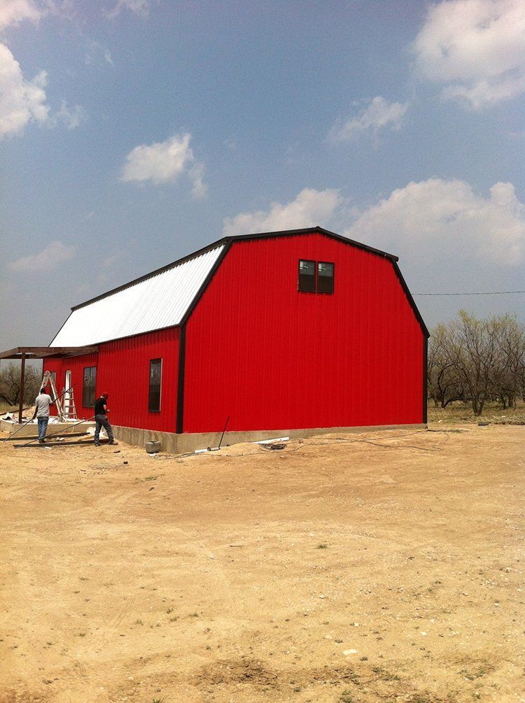 A red barn with a white roof is in the middle of a dirt field