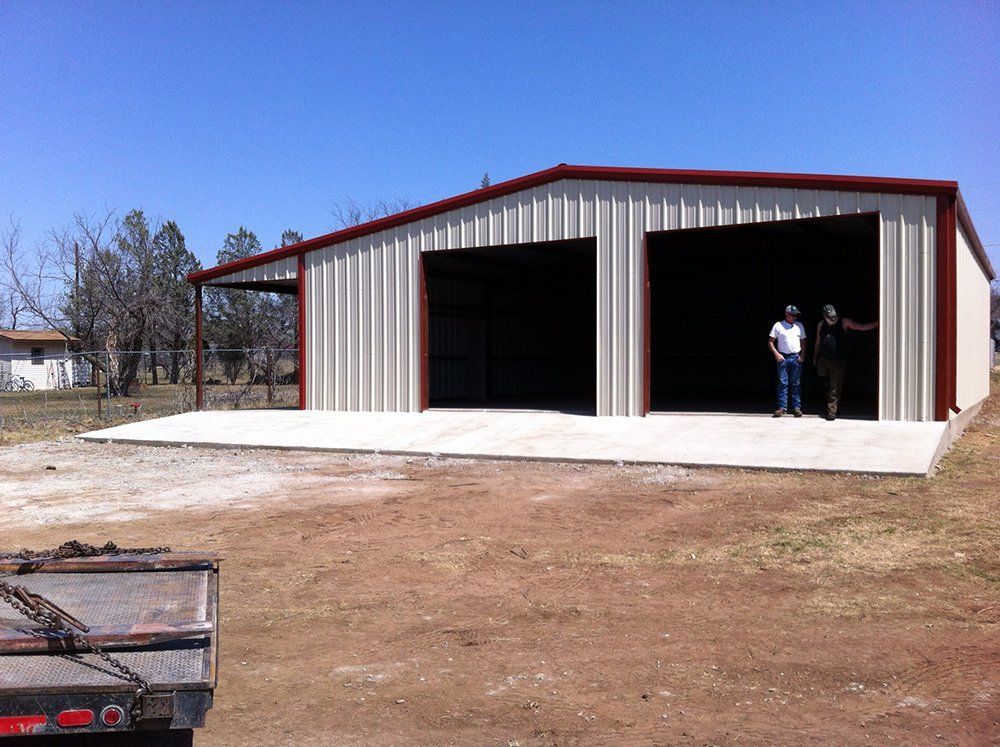 Two men are standing in front of a large metal building