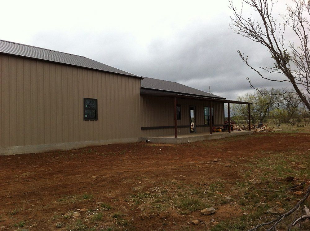 A house with a porch is sitting in the middle of a dirt field.