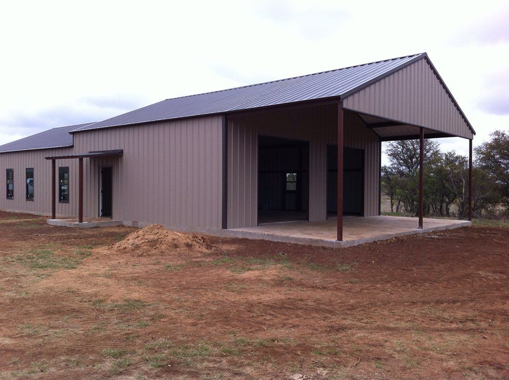 A large metal building with a porch is sitting in the middle of a dirt field.