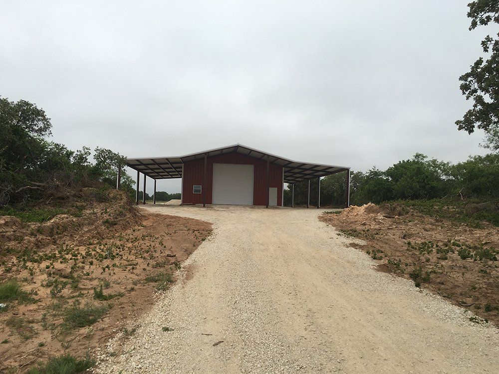 A red barn is sitting on the side of a dirt road.