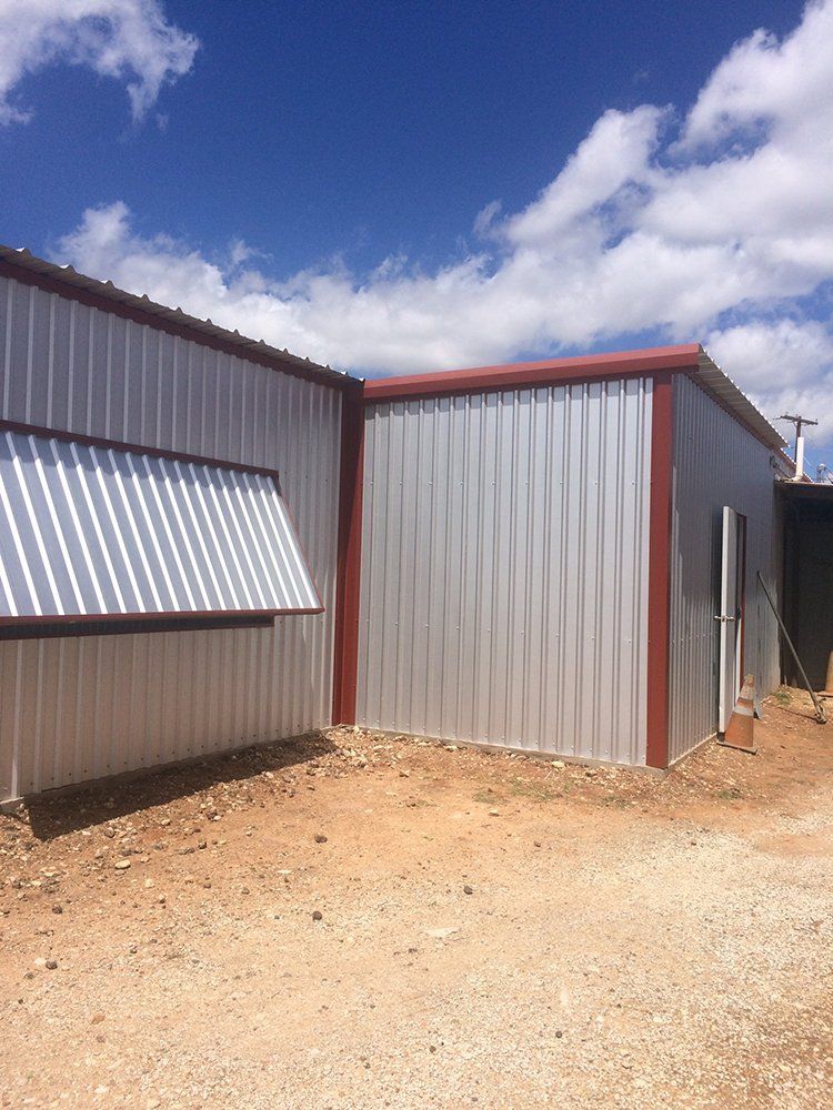 A metal building with a red roof is sitting on top of a dirt field.
