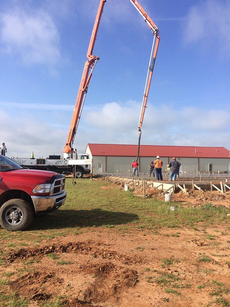 A red truck is parked in a dirt field next to a concrete pump.