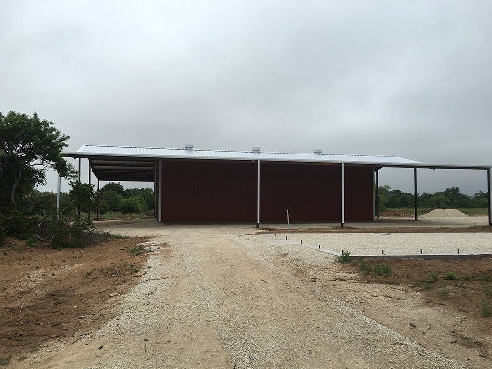 A large red barn is sitting on the side of a dirt road.