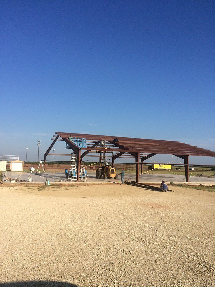 A large metal structure is being built in a gravel lot.