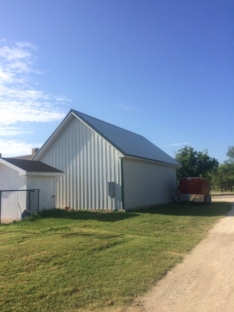 A white barn with a metal roof is sitting next to a dirt road.