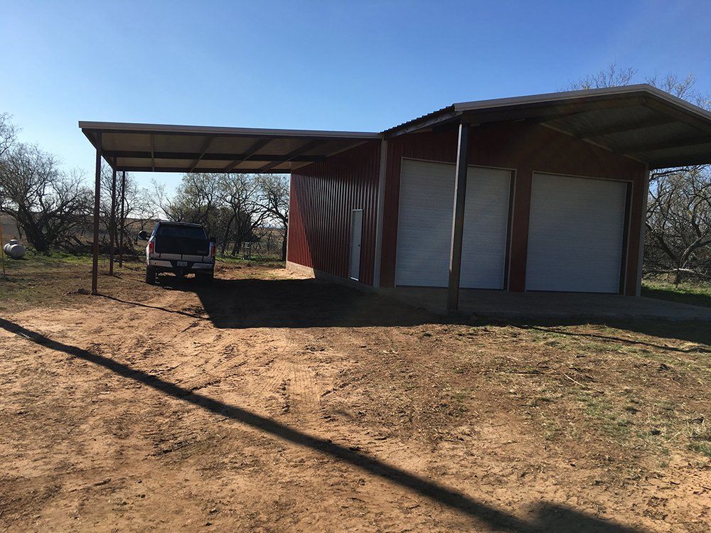 A car is parked under a canopy in front of a garage.