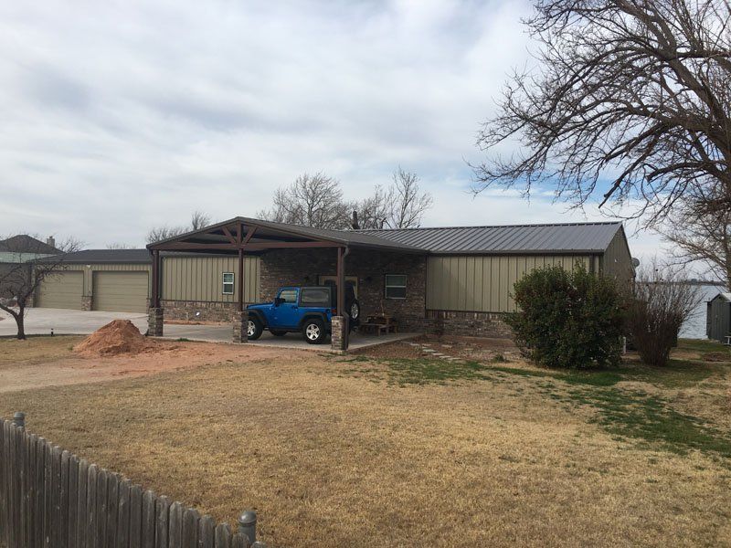 A blue truck is parked in front of a house with a carport.