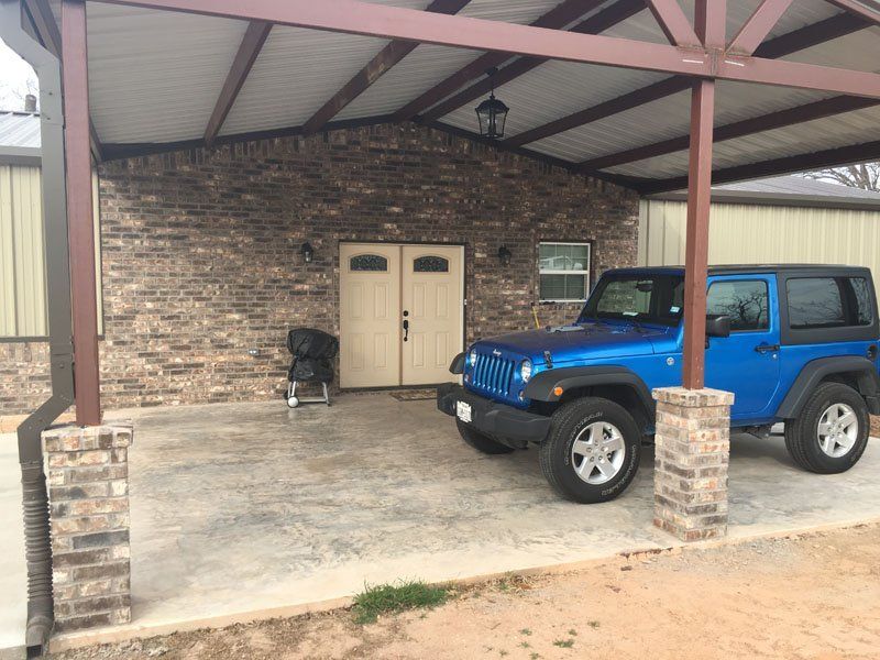 A blue jeep is parked under a covered porch