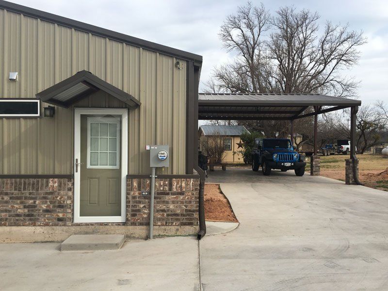 A jeep is parked under a carport in front of a house