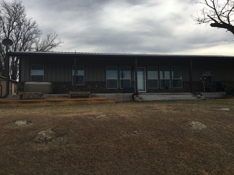 A large house with a porch and a lot of windows is sitting on top of a lush green field.