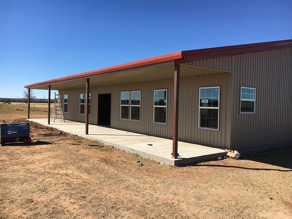 A large metal building with a red roof and a porch.
