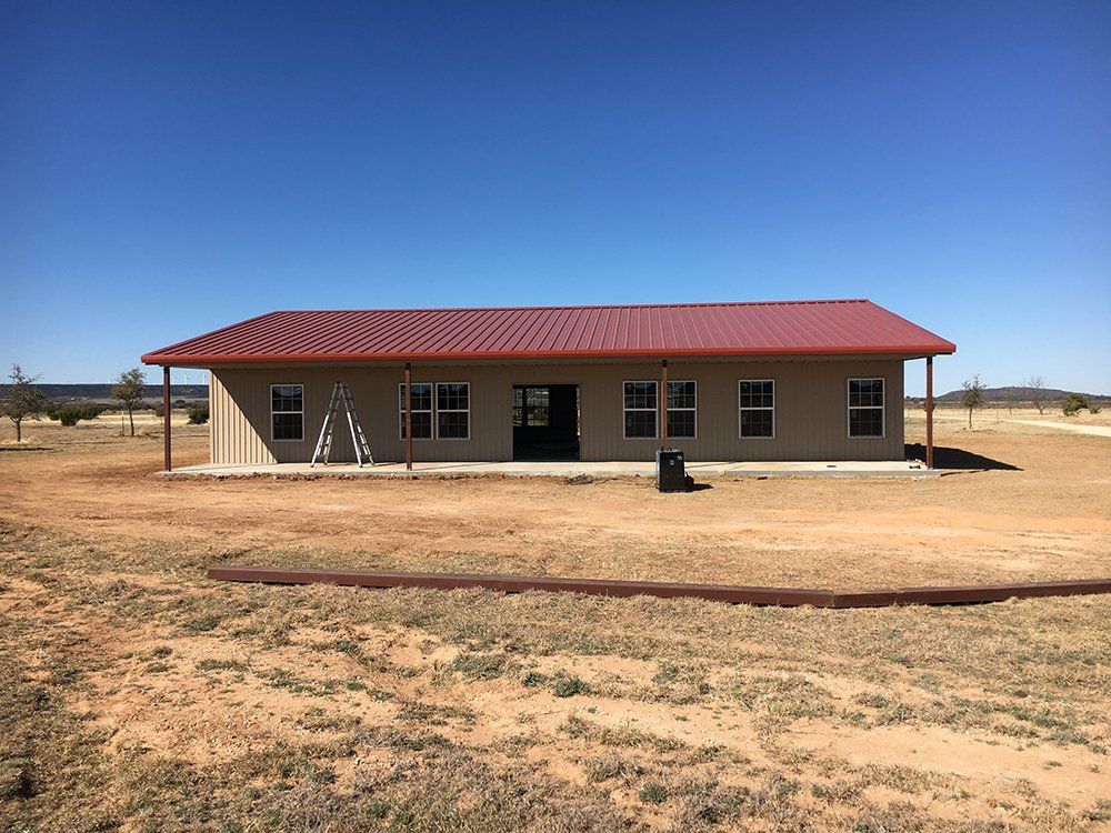 A large house with a red roof is sitting in the middle of a dirt field.