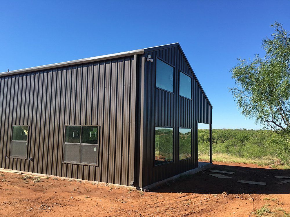 A large metal building with a lot of windows is sitting on top of a dirt field.