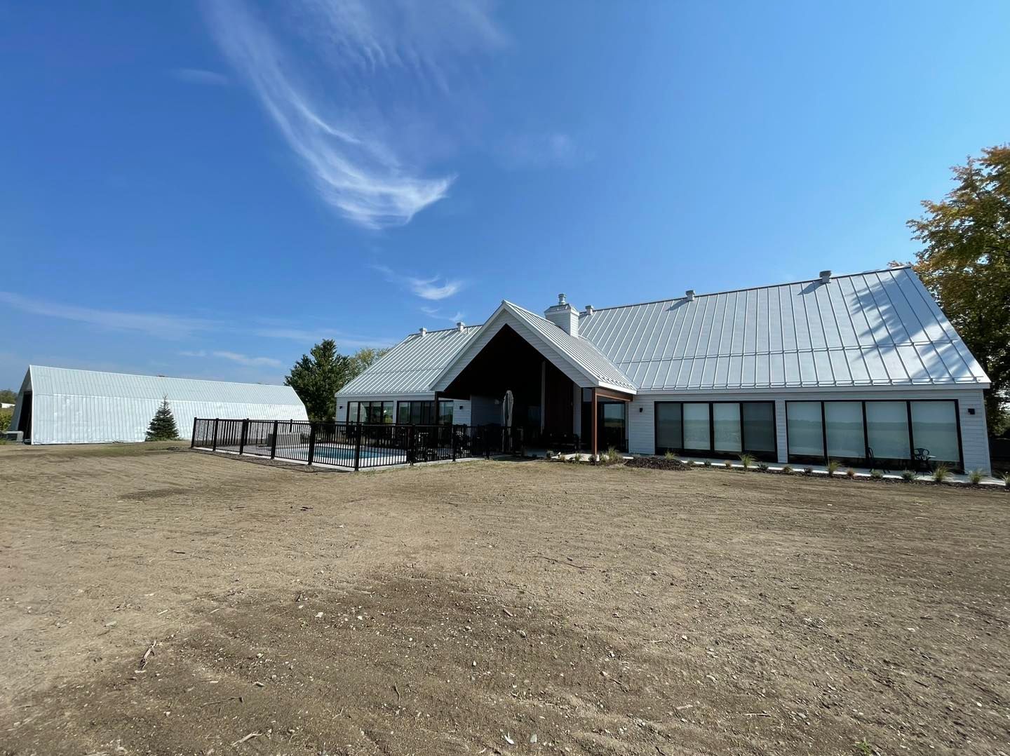 Une grande maison avec un toit en métal se trouve au milieu d'un champ de terre.
