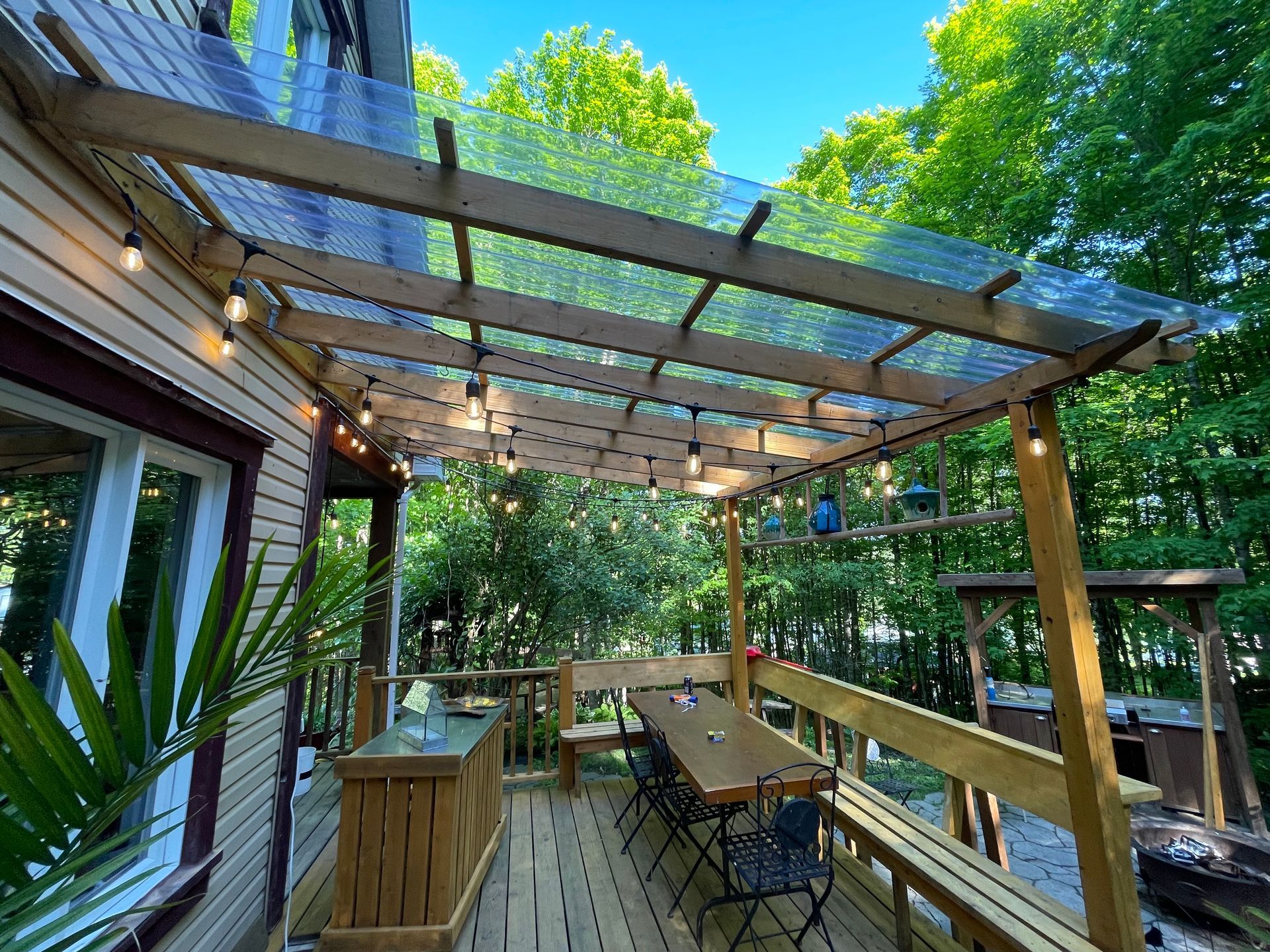 Une terrasse en bois avec une table et des chaises sous un toit transparent.