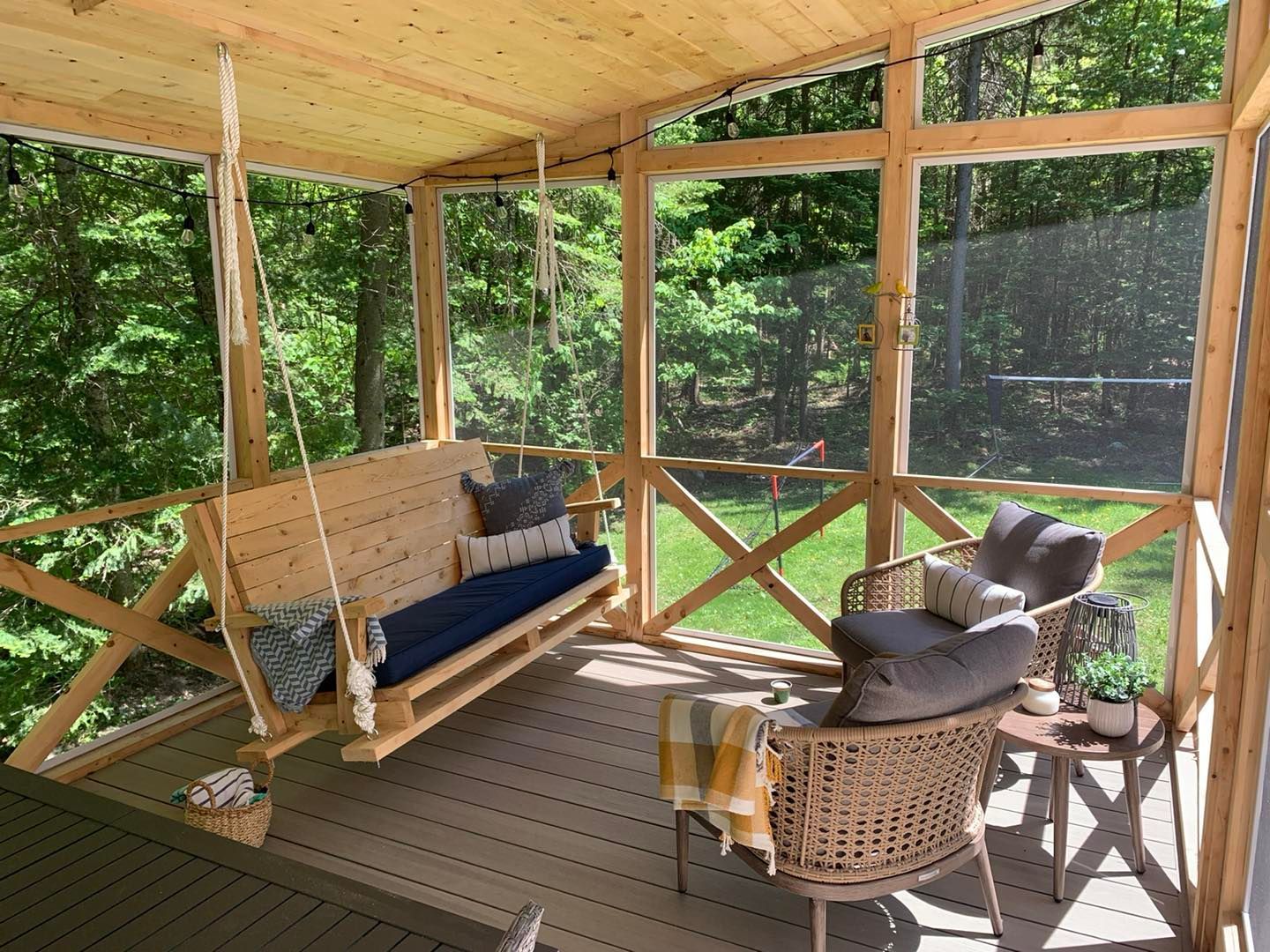 Un porche grillagé avec une balançoire et des chaises.