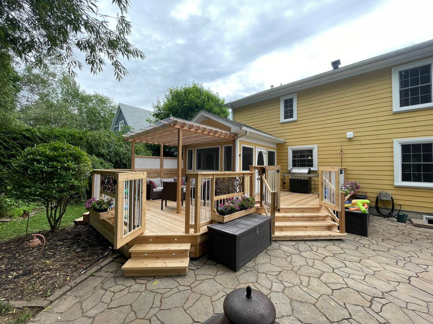 Une grande terrasse en bois se trouve devant une maison jaune.