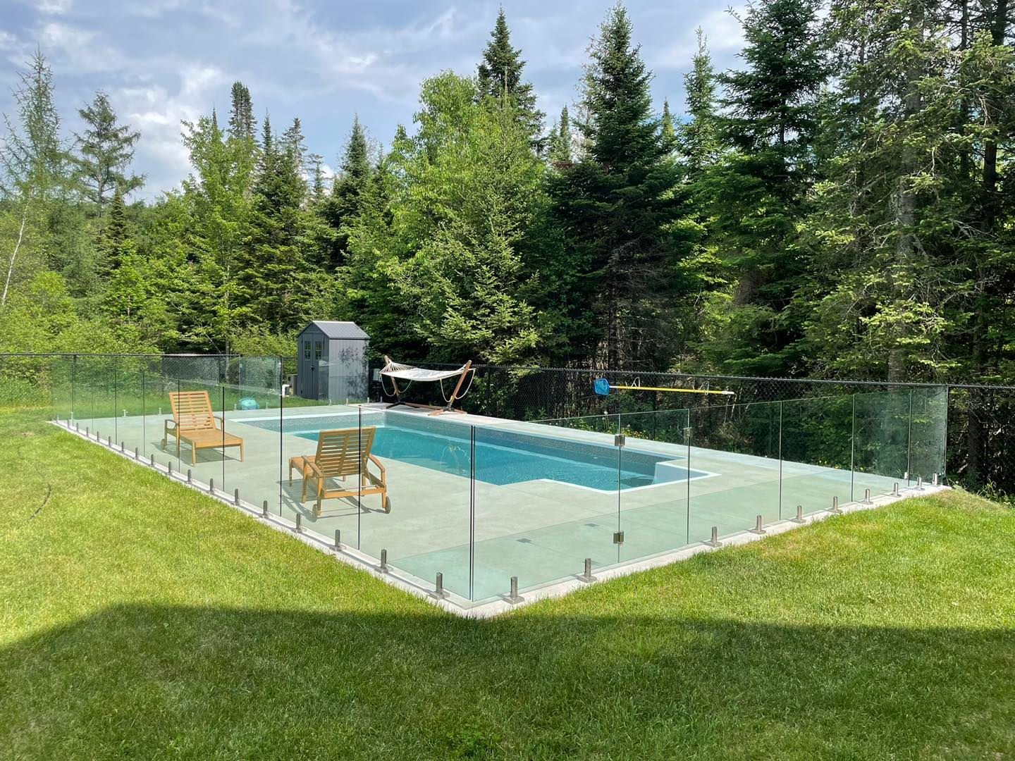 Une grande piscine entourée d'une clôture en verre dans une cour arrière.