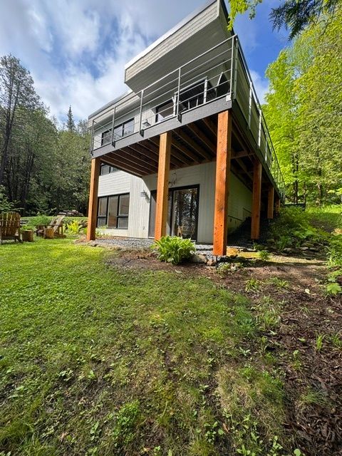 Une grande maison avec une grande terrasse est entourée d'arbres et d'herbe.