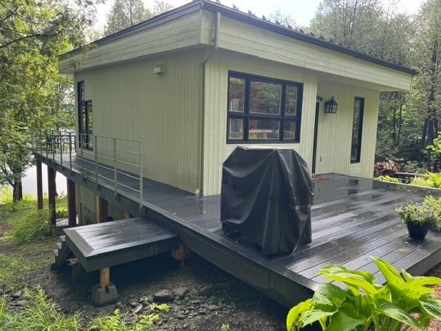 Une petite maison avec une grande terrasse et un barbecue dessus.
