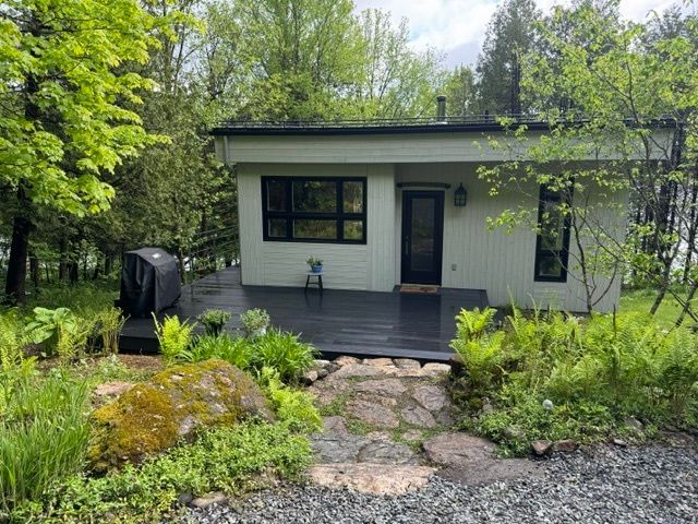 Une petite maison blanche avec une porte noire est entourée d'arbres.