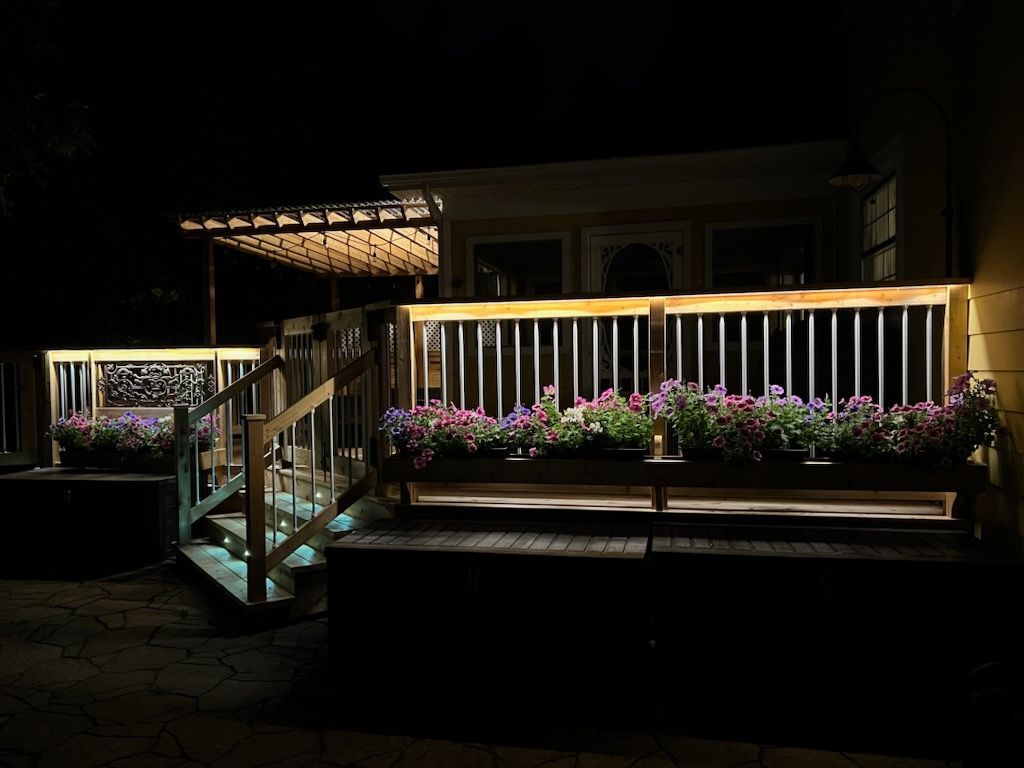 Une terrasse avec des fleurs dessus est éclairée la nuit.