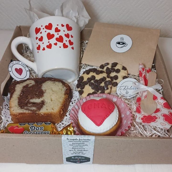 Una caja llena de una variedad de postres y una taza con corazones.