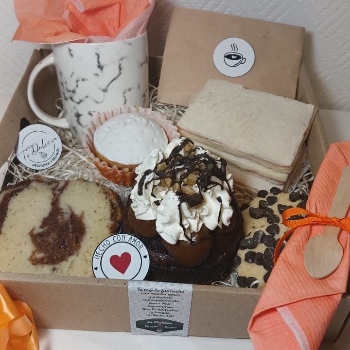 Una caja llena de pastelitos, sándwiches y una taza.