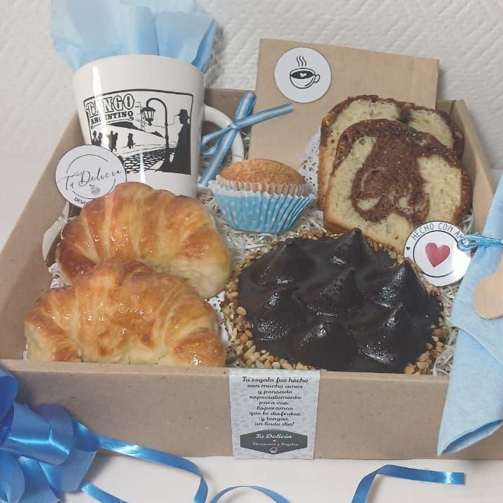 Una caja llena de croissants, cupcakes y una taza.