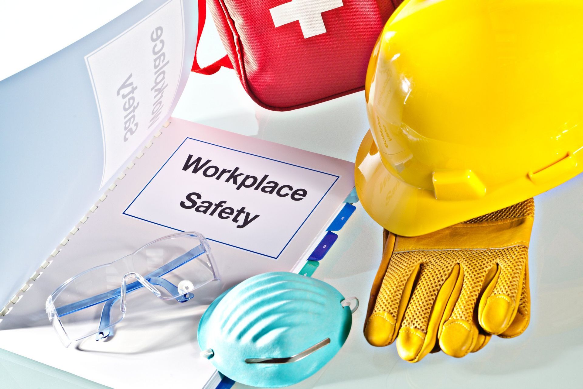 A hard hat gloves a mask a first aid kit and a workplace safety book