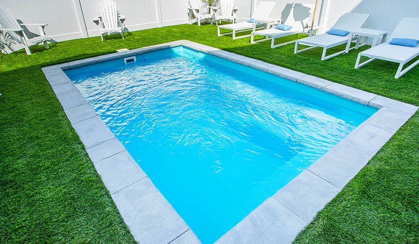 Rectangular pool with blue water, surrounded by green turf and white lounge chairs.