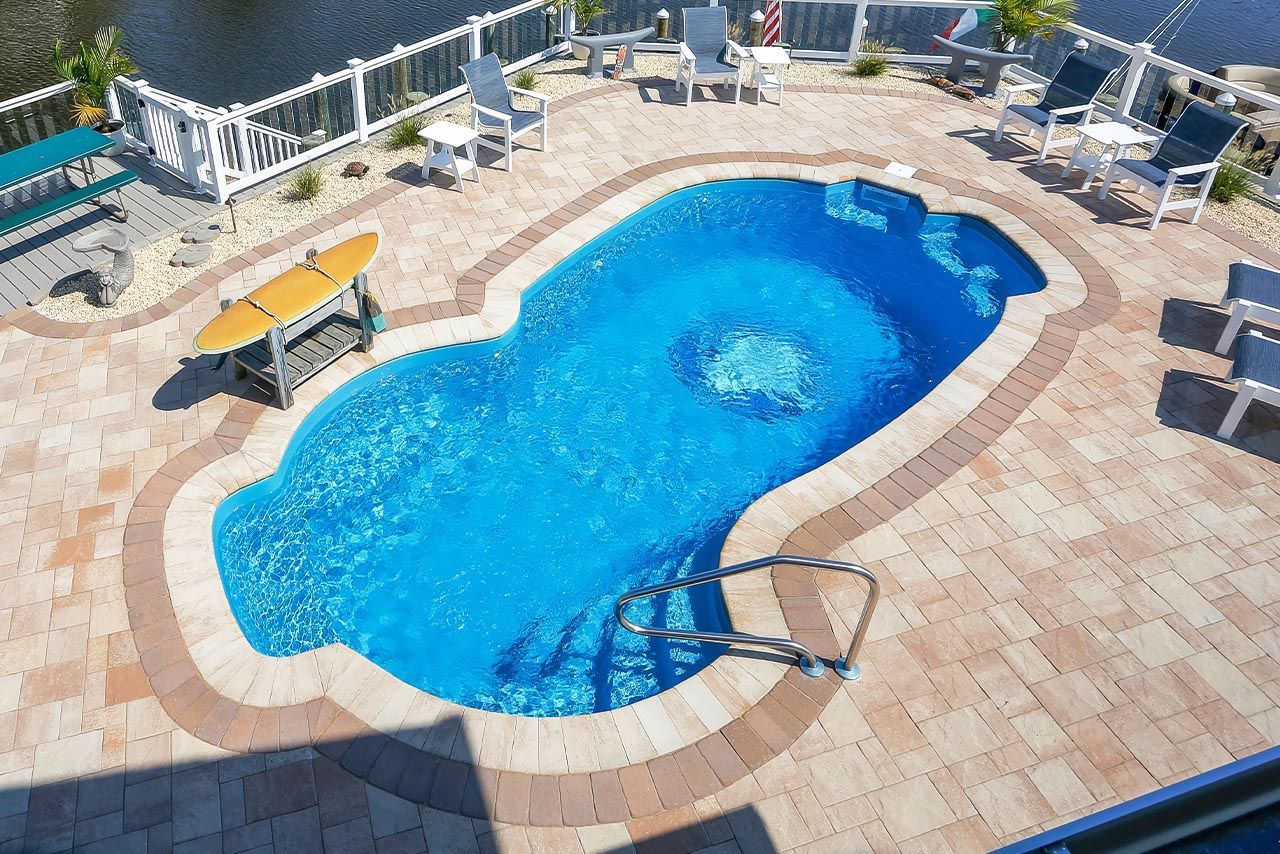 Swimming pool with curved edges, surrounded by brick patio and outdoor furniture.