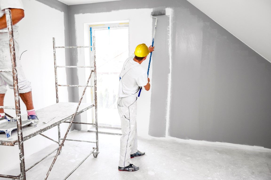 man painting interior walls grey with a paint roller