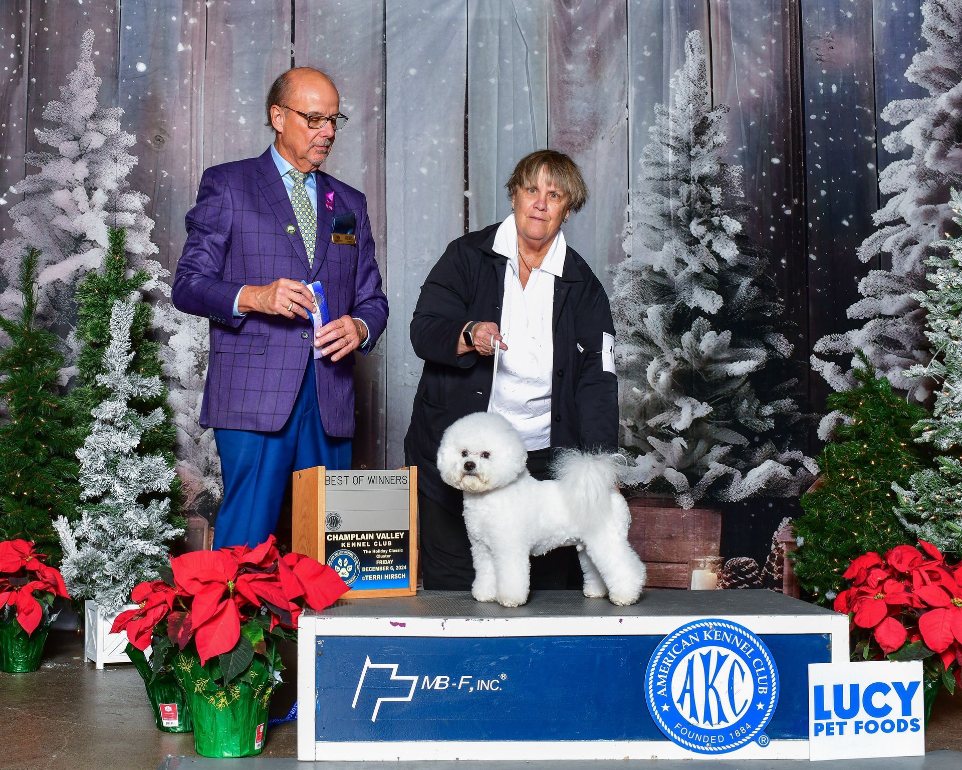 A man and woman are standing next to a small white dog.