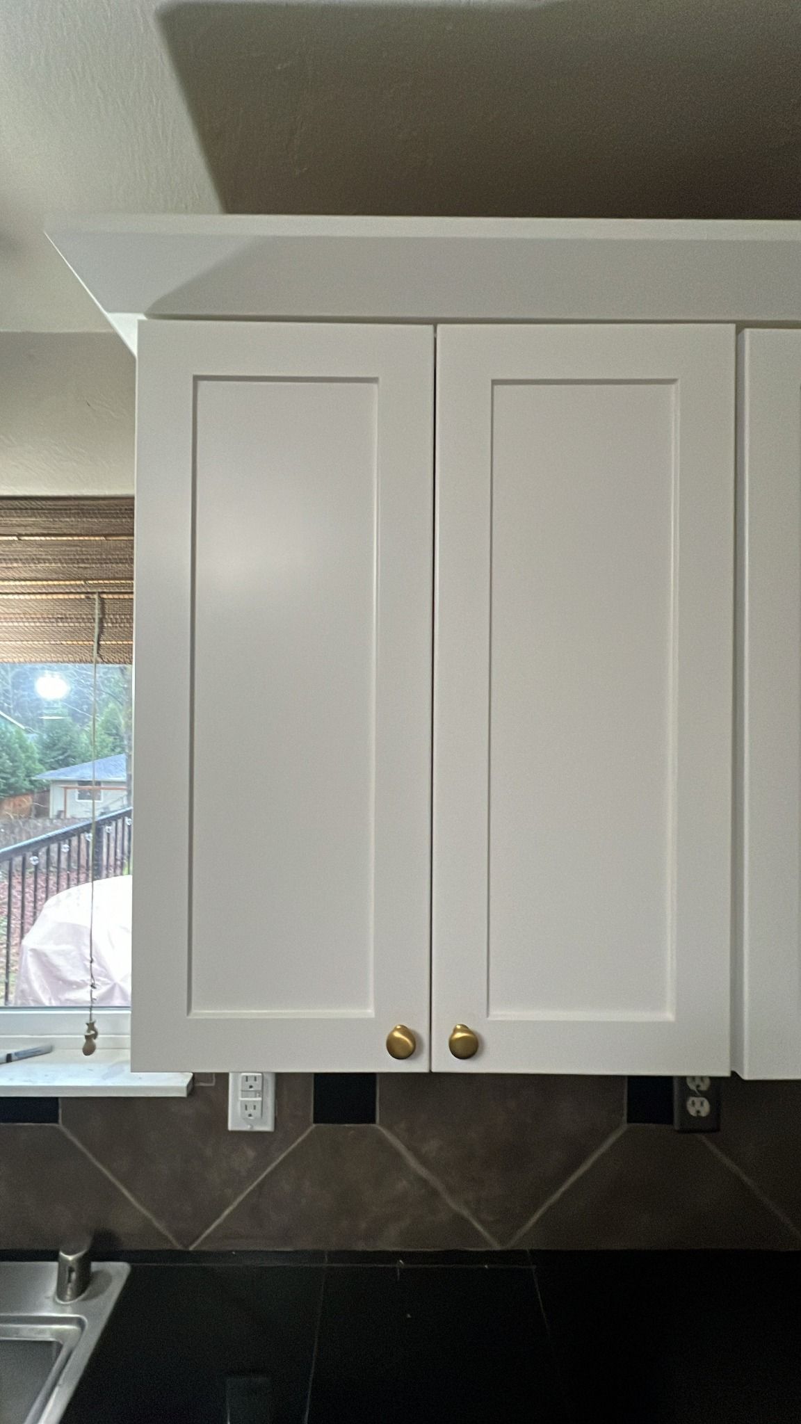 White kitchen cabinets with gold knobs above a dark countertop and tile backsplash.