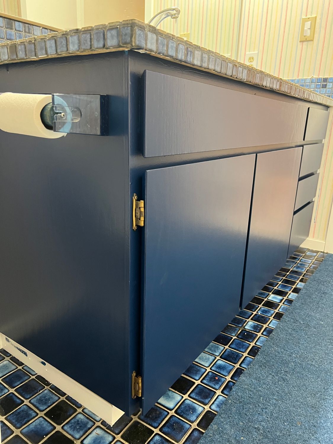 Blue bathroom vanity with a granite countertop, blue tile flooring, and a toilet paper holder.