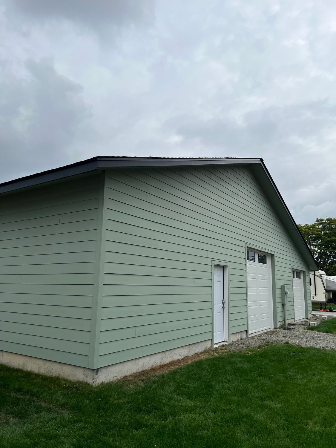 Green building with white garage doors and a small door, green siding, under a cloudy sky.