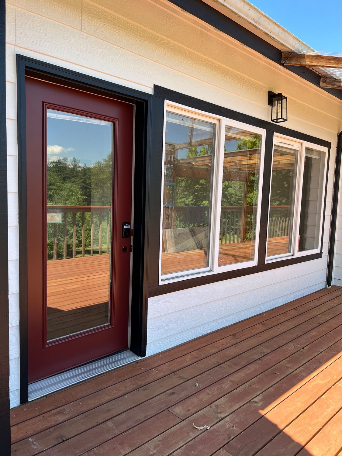 Red door and windows on a white and black trimmed building with a wooden deck.