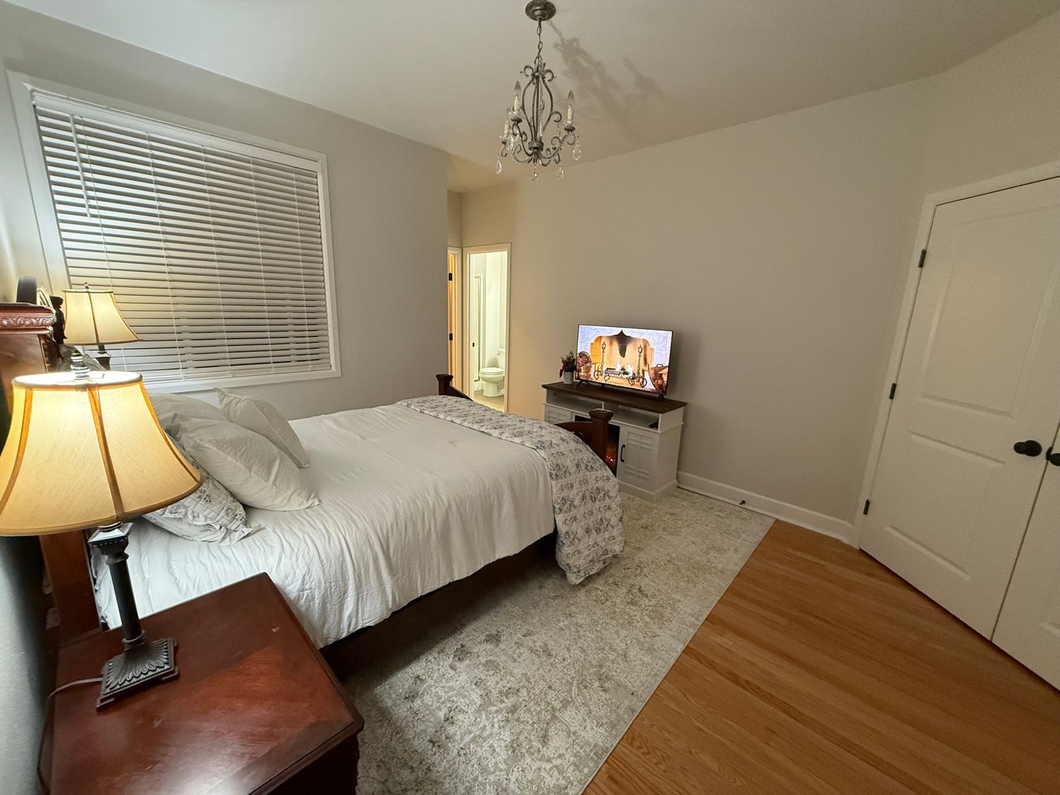 Bedroom with a bed, TV, lamps, and a door.