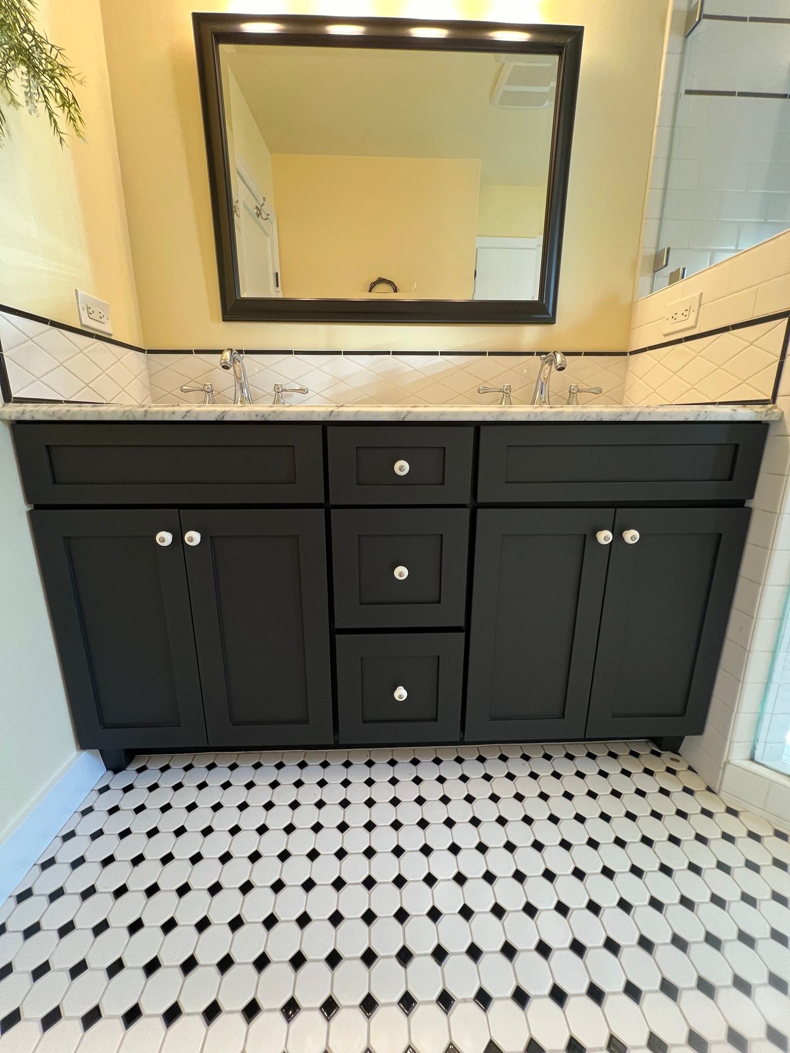 Black bathroom vanity with a black framed mirror and black and white patterned floor.