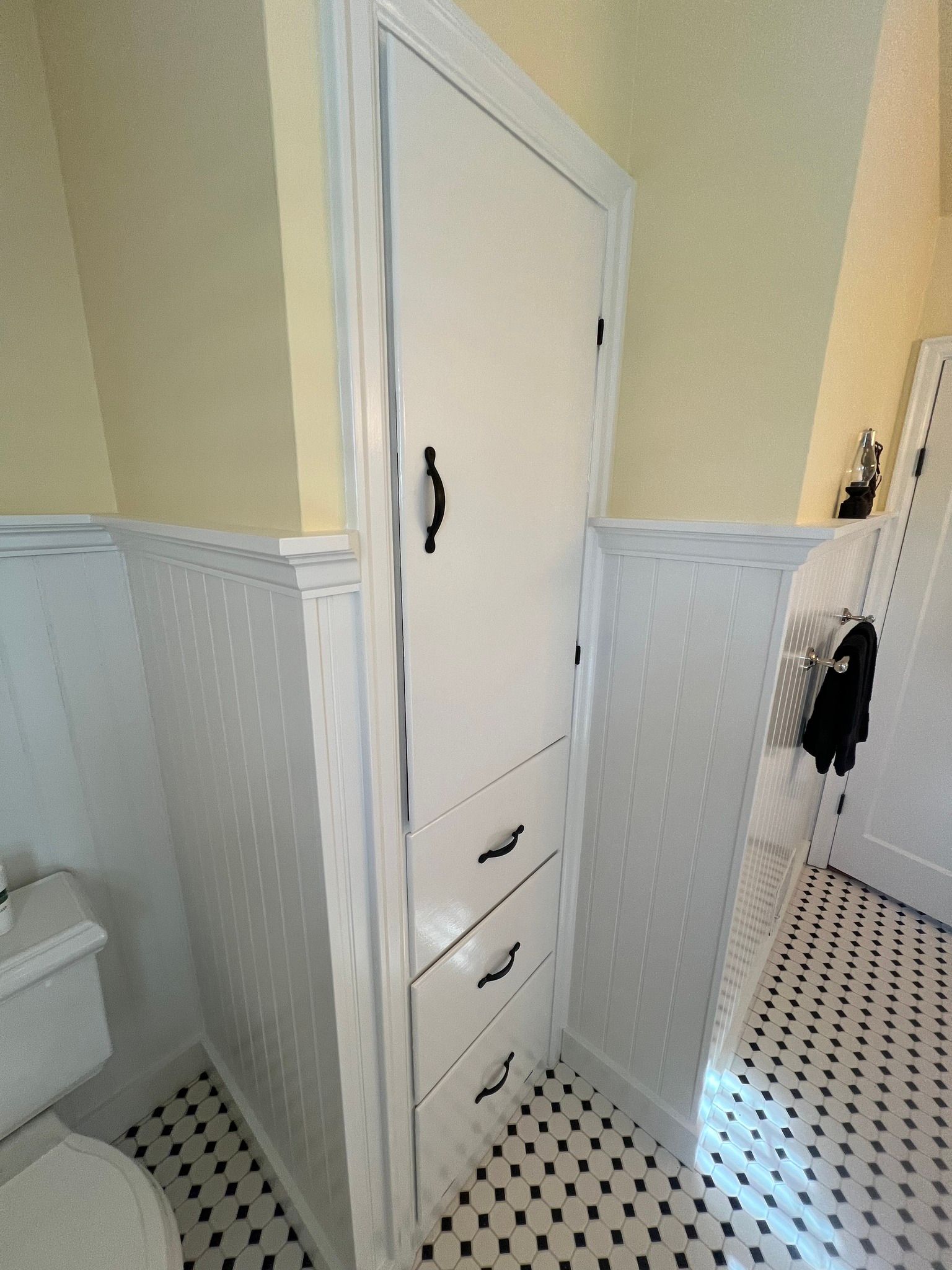 Bathroom with white cabinetry, black and white tile flooring, and a toilet.